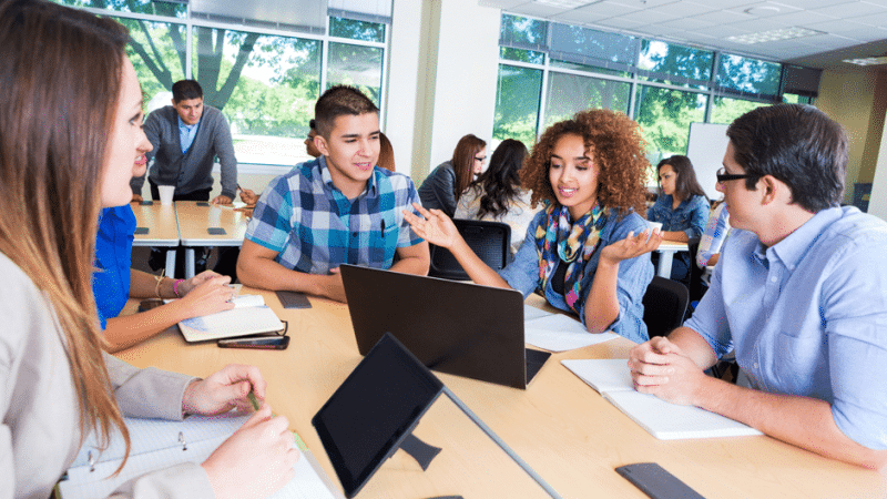 High school aged students sitting around a table having a discussion.